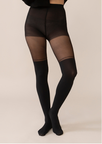A model wearing sheer black thigh-high stockings with opaque black lower legs, paired with a black knit sweater, shown from the front against a solid light beige background.