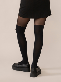 Back view of a person wearing Scalloped over-the-knee black tights paired with a black skirt and black shoes.